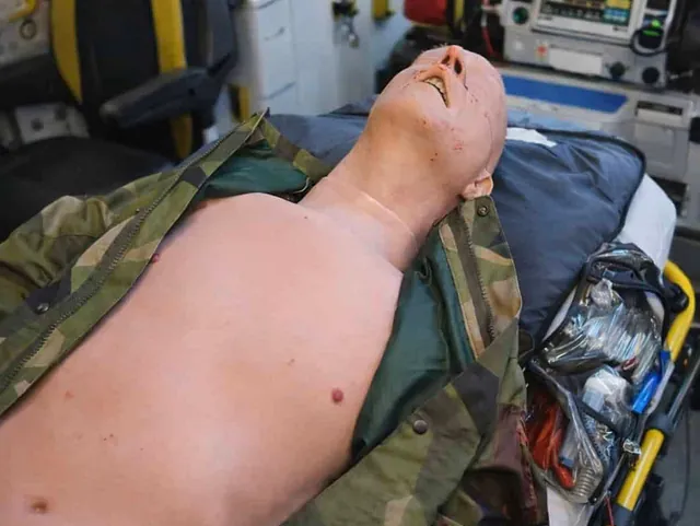 Øvingsdukke med simulerte skader ligger på båre i ambulanse under trening i akuttmedisin.